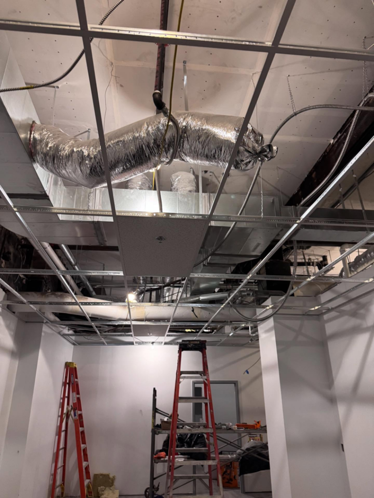 An interior commercial space under construction with exposed HVAC ducts, ceiling grid, and ladders by Russell General Contracting, LLC in Pittsburgh, PA.