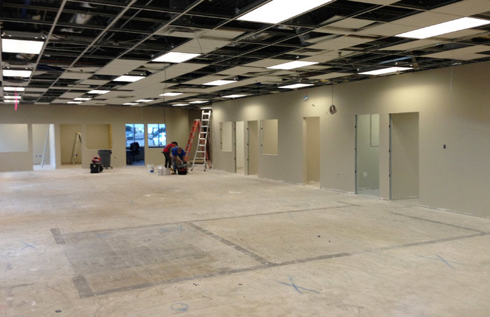 Workers performing interior renovation tasks with ladders and exposed ceiling grid in a commercial space by Doege Development, LLC in Phoenix, AZ.