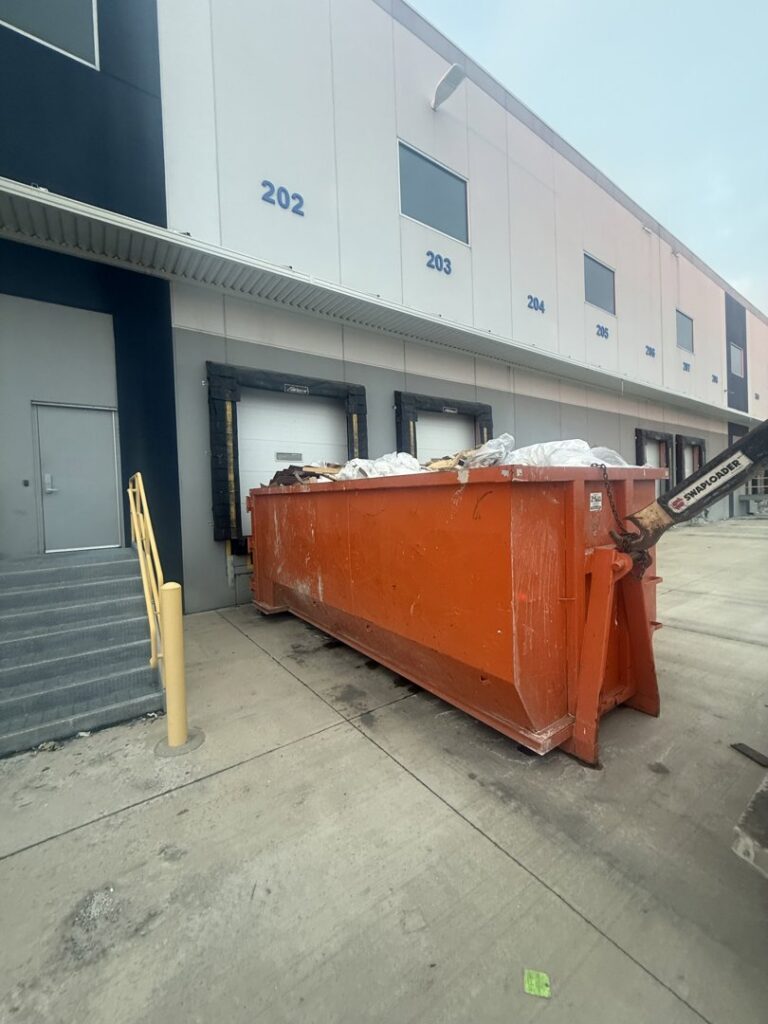 An orange dumpster filled with commercial junk next to a loading dock, handled by Lil Man W/A Can LLC in Columbus, OH.