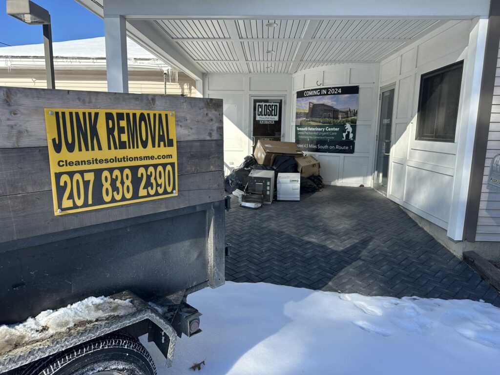 A commercial junk removal trailer with a 'JUNK REMOVAL' sign, collecting items for CleanSite Solutions in Windham, ME.