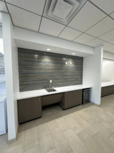 A newly installed commercial kitchenette with sink, cabinets, and tiled backsplash by Bayou State Commercial Flooring in Monroe, LA.