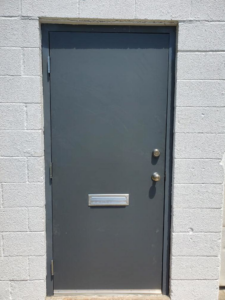 A grey commercial metal door installed in a white cinder block wall by Lucas Overhead Doors, a general contractor in Erie, PA