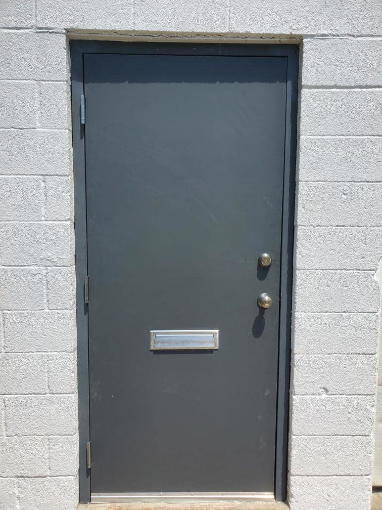 A grey commercial metal door installed in a white cinder block wall by Lucas Overhead Doors, a general contractor in Erie, PA