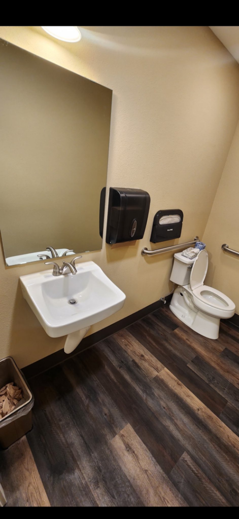 A commercial restroom featuring a wall-mounted sink, mirror, and grab bars installed by Leupitz Contractors Inc in Salem, OR.