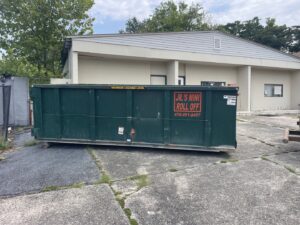 A green roll-off dumpster from Jr's Mini Roll Off LLC in a commercial parking lot in Byron, GA.