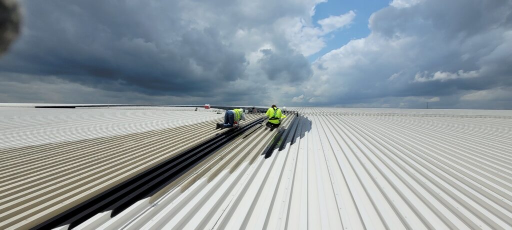 Workers applying a protective coating to a large commercial roof, a service provided by T-Byrd Painting in Austin, TX