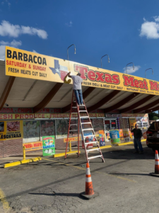 A worker on a ladder installing or repairing a commercial sign for Texas Meat Market by DeLeon Contracting LLC in San Antonio, TX.