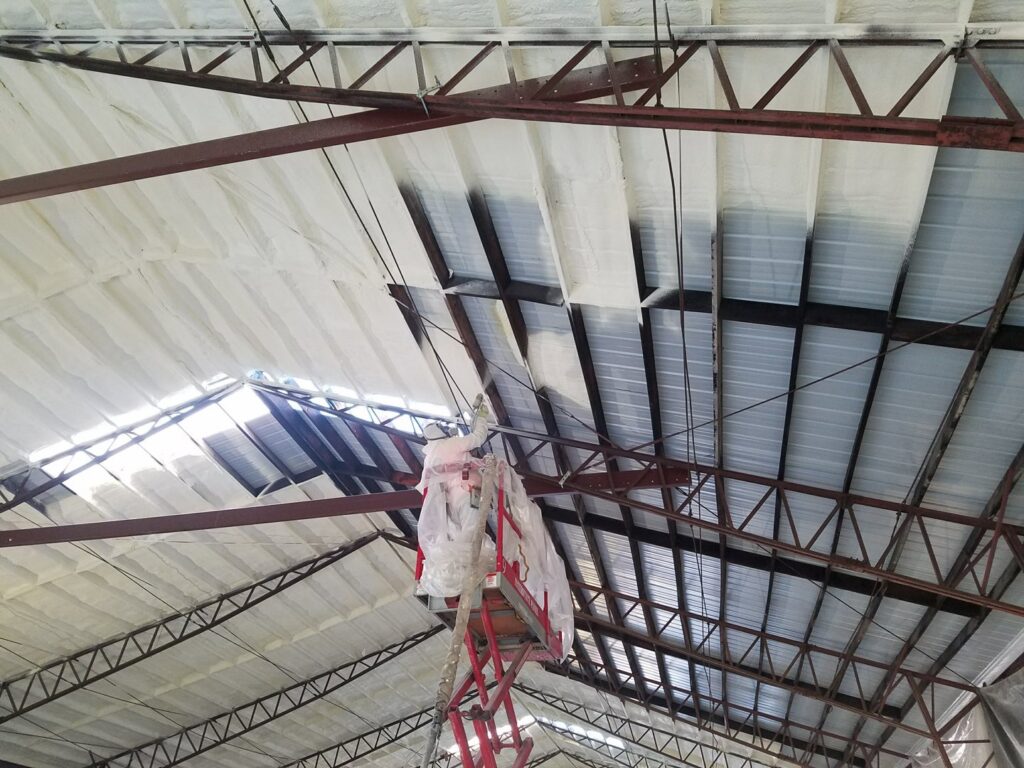 A worker on a lift applying spray foam insulation to a commercial building ceiling for Absolute Pro Insulation in Corpus Christi, TX.