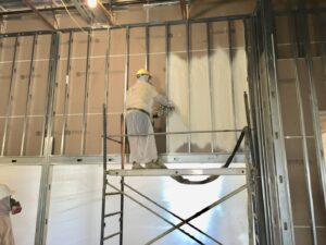A worker on scaffolding applying spray foam insulation to a commercial building wall by Spray Foam Art-Insulation in Stamford, CT.