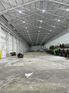 A brightly lit commercial warehouse interior, showcasing new overhead lighting installed by JR Insulation Services in Cleveland, OH.