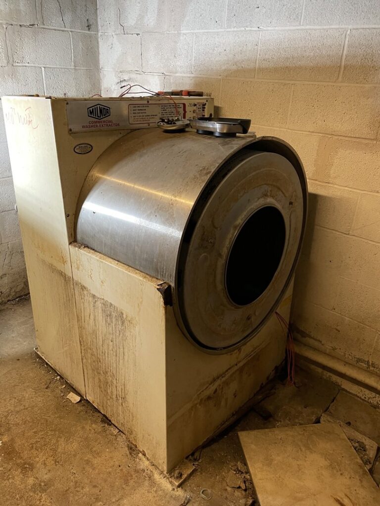 A large, old commercial washer extractor in a basement, ready for removal by Nu Earth Hauling and Recycling in Allentown, PA.