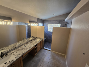 A complete bathroom renovation featuring a double vanity with granite countertops and a newly tiled shower by Next Level Finish in Fort Collins, CO.