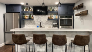 A beautifully completed basement bar with dark cabinets, white countertop, tile backsplash, and modern appliances by Yellow Ladder Contracting in Mount Pleasant, SC