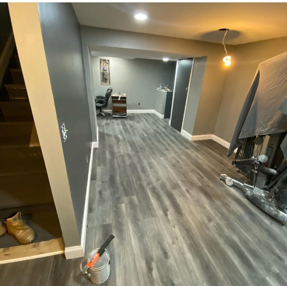A newly renovated basement with grey wood-look flooring and fresh paint by Jarrett's Home Improvements & Maintenance Services in Columbus, OH
