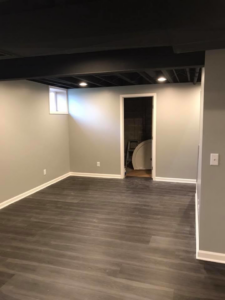 A completed basement room with dark flooring and light gray walls, showing a doorway, by M Zimmer Construction LLC in Rochester, NY.