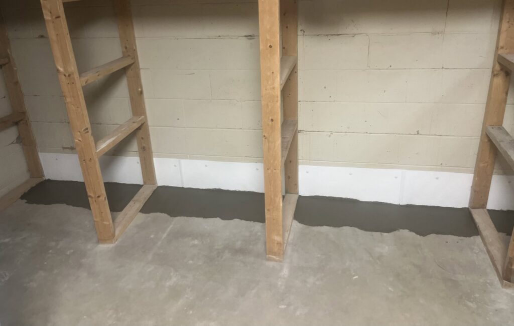 A section of a basement wall with completed interior waterproofing and fresh concrete sealant by TCM Waterproofing, LLC in Canton, OH.