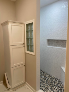 A completed bathroom remodel with a tall white cabinet, glass block window, and newly tiled shower by DG Pro Remodeling in Charlotte, NC