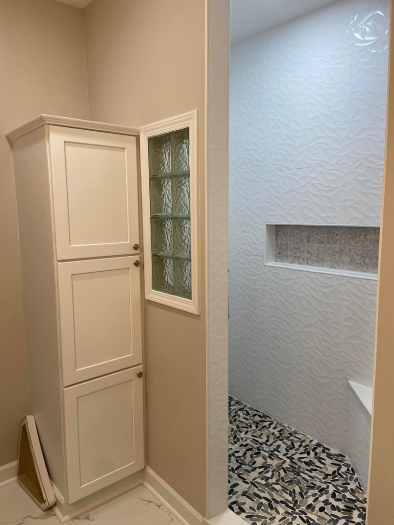 A completed bathroom remodel with a tall white cabinet, glass block window, and newly tiled shower by DG Pro Remodeling in Charlotte, NC