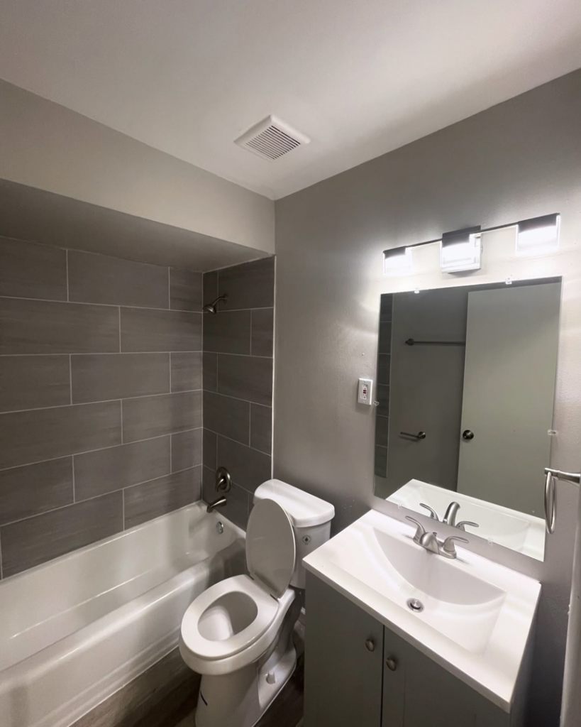A newly remodeled bathroom with modern gray tiles, new vanity, and toilet by Make It Happen Homes STL in St. Louis, MO.