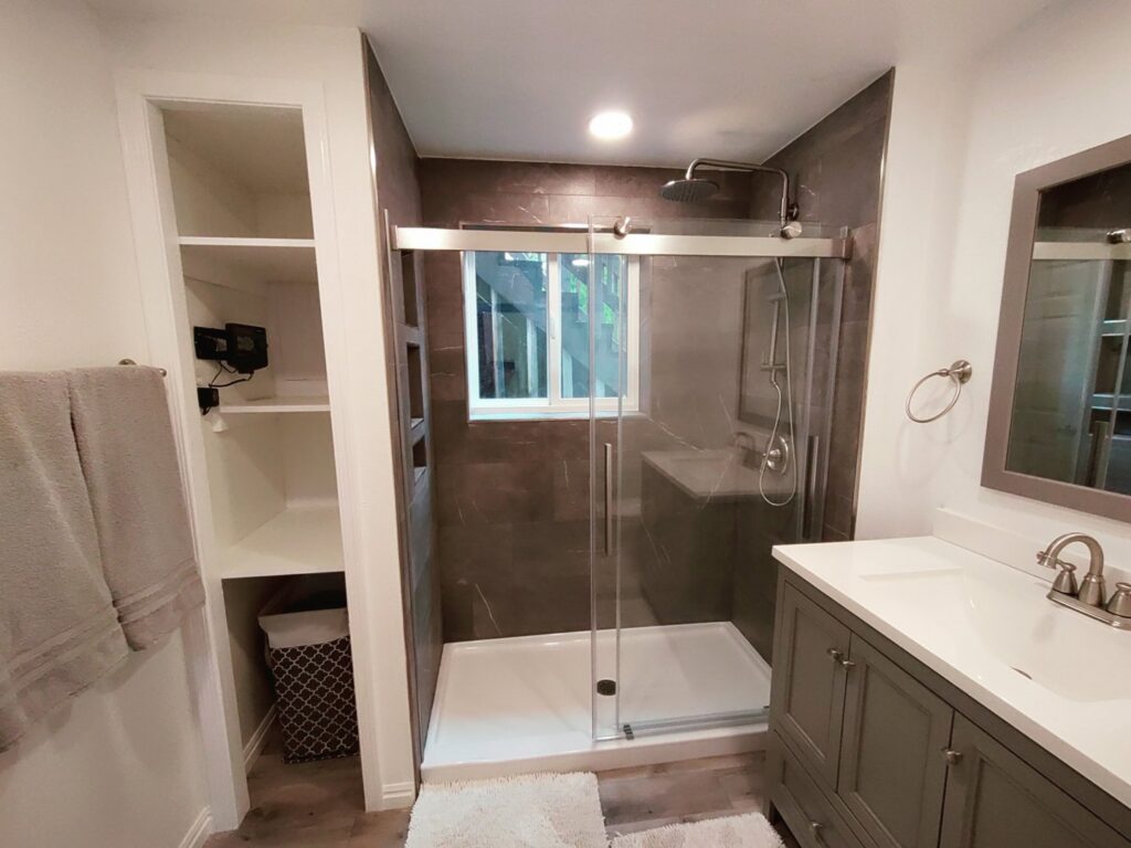 A completed bathroom remodel featuring a dark tiled shower with glass enclosure, vanity, and built-in shelving by Devco Construction LLC in West Valley City, UT.