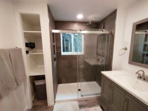 A completed bathroom remodel featuring a dark tiled shower with glass enclosure, vanity, and built-in shelving by Devco Construction LLC in West Valley City, UT.