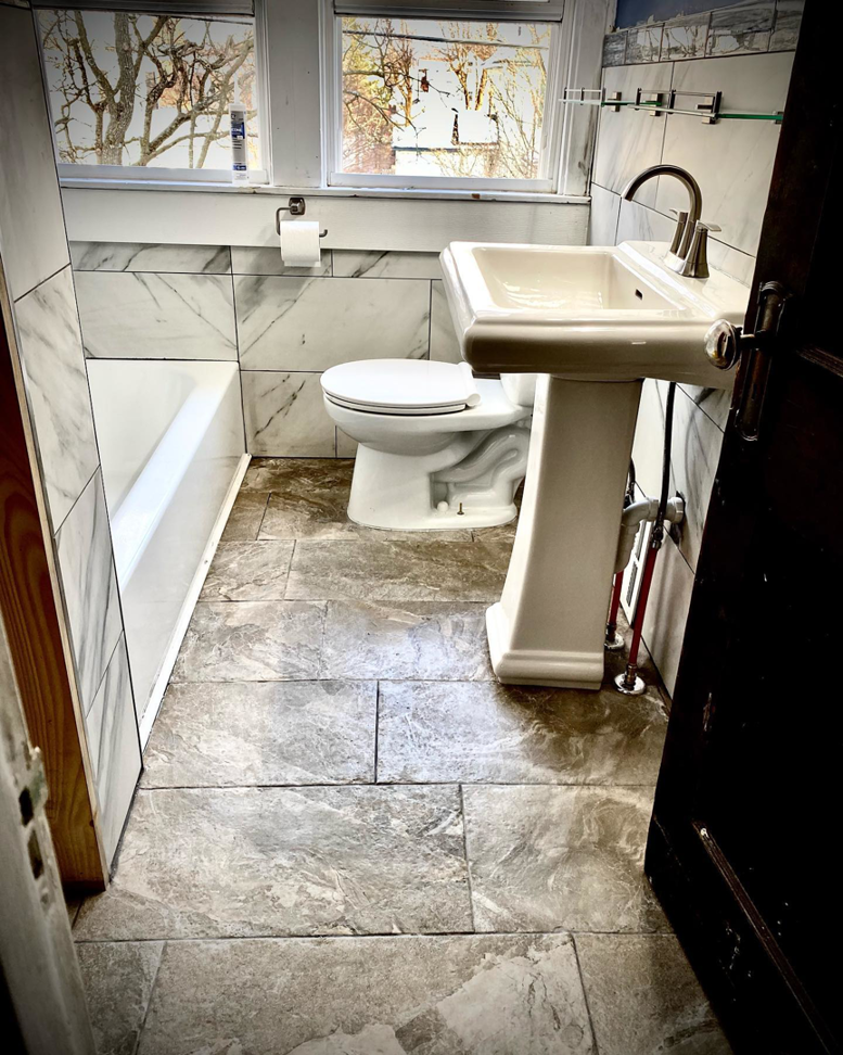 A beautifully completed bathroom remodel with marble-look tiles and new fixtures by Mohawk Home Improvement of Syracuse LLC in Syracuse, NY.