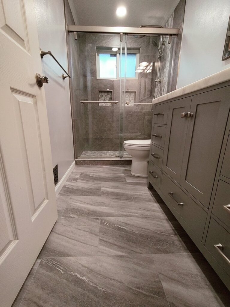 A beautifully completed bathroom remodel featuring a large vanity, toilet, and a walk-in shower with glass doors by Devco Construction LLC in West Valley City, UT.