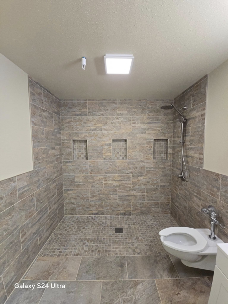A beautifully completed bathroom renovation featuring a new tiled walk-in shower and toilet by Torres Services in Anchorage, AK.
