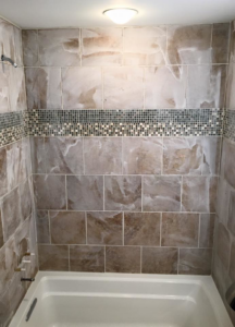 A completed bathroom shower tiling project with brown tiles and a decorative mosaic band by I'll Fix It in Shawnee, KS.