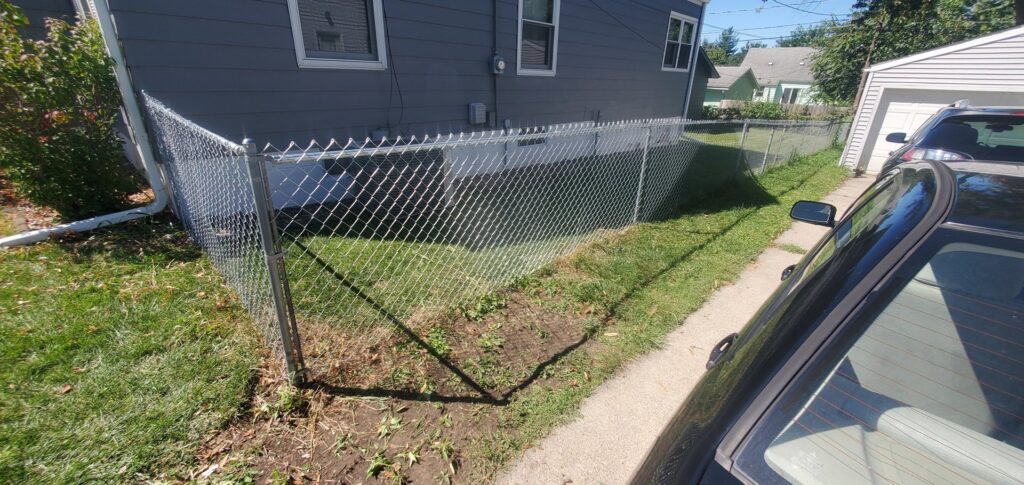 A newly installed chain-link fence in a residential yard by Justin-case Repairs in Ankeny, IA.