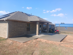 A newly completed concrete patio extension next to a brick house, built by All American Concrete in Crescent, OK.