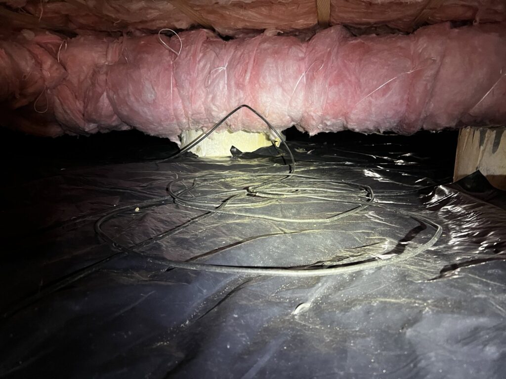 A view of a completed crawl space project with a black vapor barrier, pink insulation, and electrical wiring, installed by Northwest Crawl Space Services in Kent, WA.