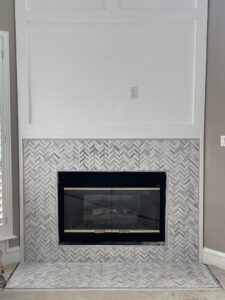 A completed fireplace renovation featuring a herringbone tile surround and a white mantel by Brewer Builds in Fort Worth, TX.