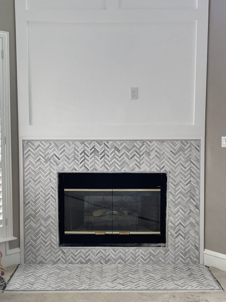A completed fireplace renovation featuring a herringbone tile surround and a white mantel by Brewer Builds in Fort Worth, TX.