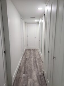 A renovated hallway with new light grey wood-look flooring and fresh white walls, completed by Stormtroopers Home Improvement in Port St. Lucie, FL.