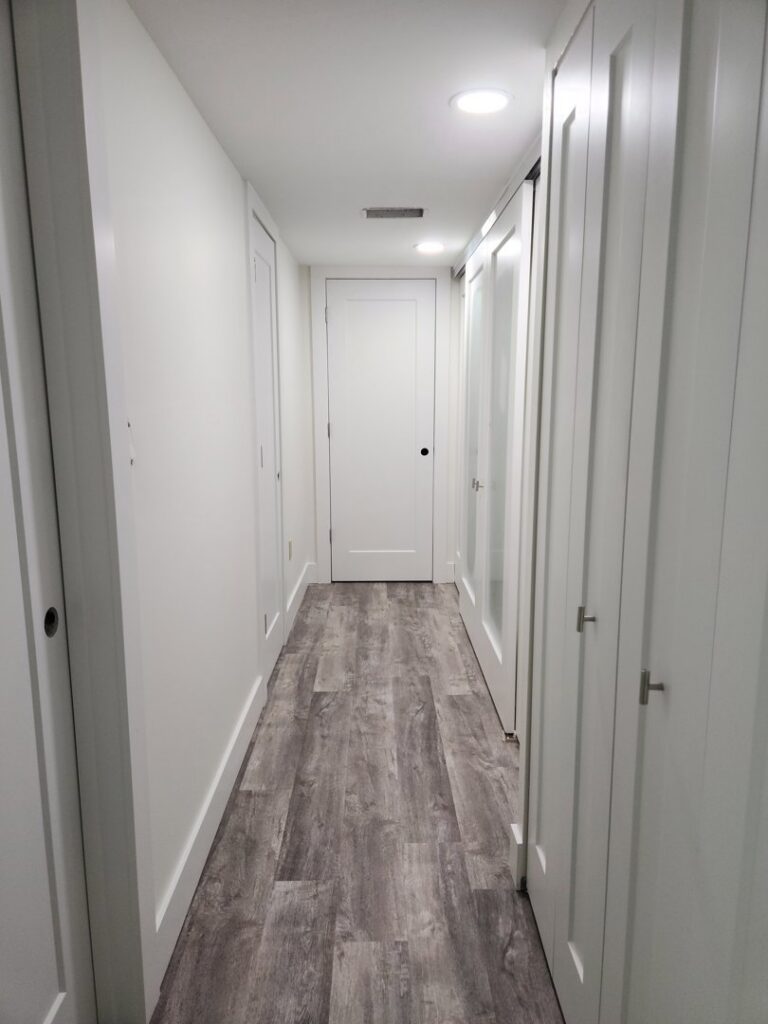 A renovated hallway with new light grey wood-look flooring and fresh white walls, completed by Stormtroopers Home Improvement in Port St. Lucie, FL.
