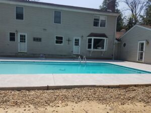 A completed inground pool with new concrete decking next to a residential home by My Pool Guys of Erie, PA.