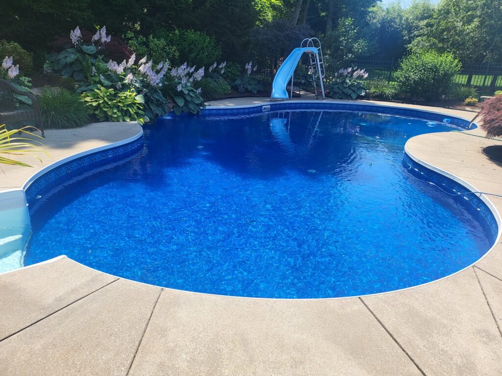 A beautifully completed inground pool with a blue liner, slide, and concrete patio by My Pool Guys of Erie, PA.