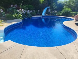 A beautifully completed inground pool with a blue liner, slide, and concrete patio by My Pool Guys of Erie, PA.