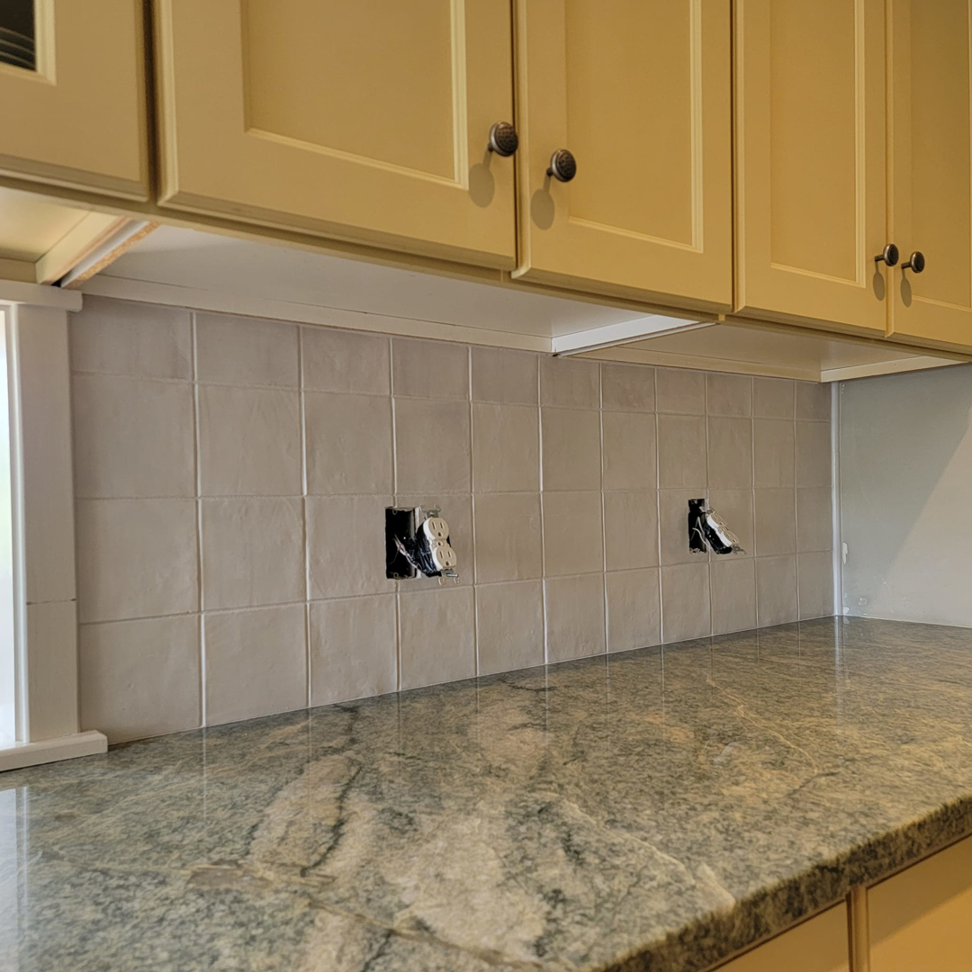 A newly completed kitchen backsplash with white tiles and granite countertops by Jonny Hinton - Handyman Extraordinaire in Colorado Springs, CO.