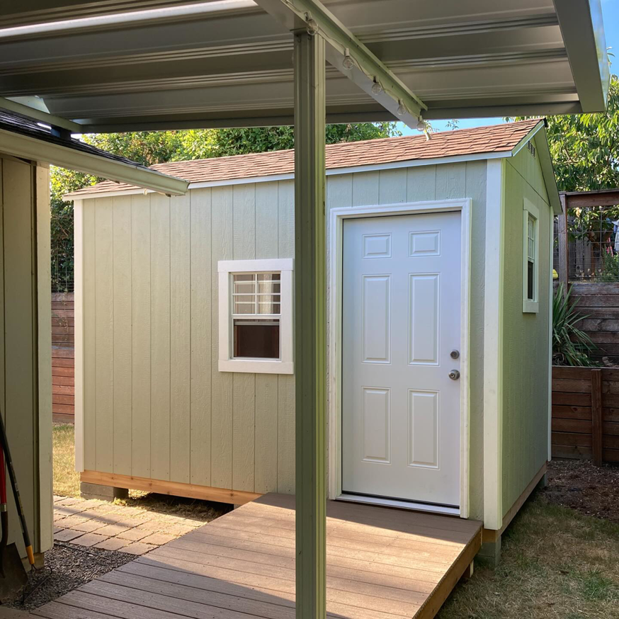 A completed light-colored shed featuring a new door, window, and wooden access ramp by Shed Crafters in Sycamore, IL