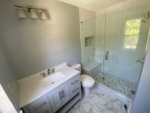 A completed modern bathroom featuring a vanity, toilet, and walk-in shower with pebble flooring by Stonehedge Construction in Buford, GA