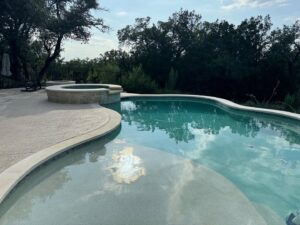 A completed swimming pool and hot tub with surrounding patio and landscaping by 5 Daughters Total Outdoors in Austin, TX.