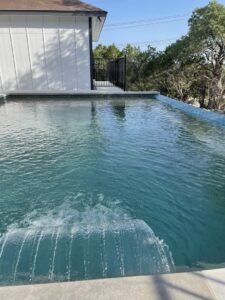 A close-up of a completed swimming pool with a waterfall feature by 5 Daughters Total Outdoors in Austin, TX.