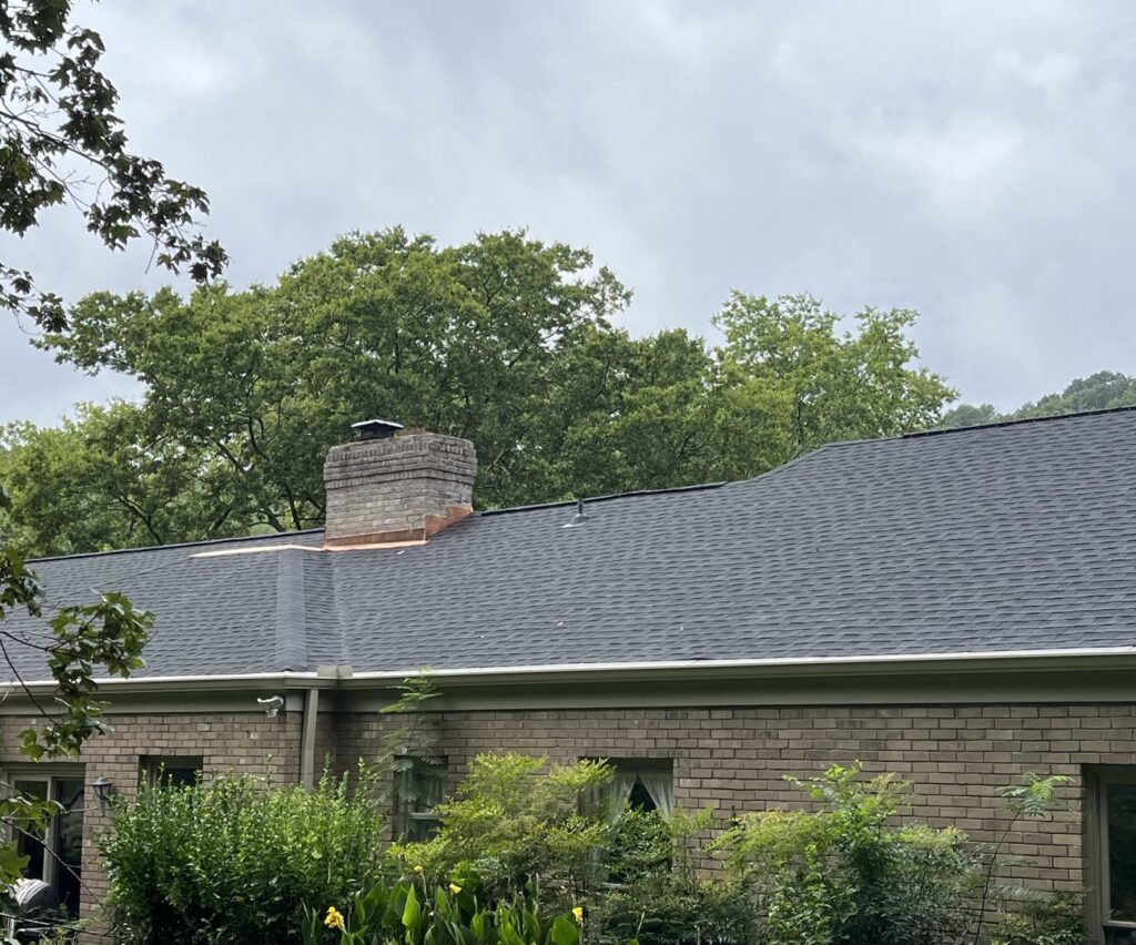 A beautifully completed dark shingle roof with a brick chimney, installed by Music City Exteriors in Nashville, TN