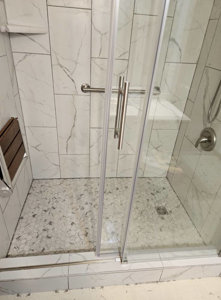 A completed tiled shower enclosure with a new glass door and hexagonal floor tiles by Tim's handyman service in Cherry Hill, NJ.