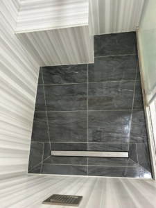 A newly completed tiled shower floor with a modern linear drain installed by Form Fluent in Kodiak, AK.