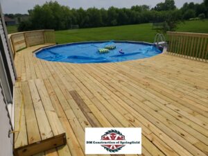 A spacious completed wooden deck built around an above-ground swimming pool, by DM Construction of Springfield in Springfield, IL.
