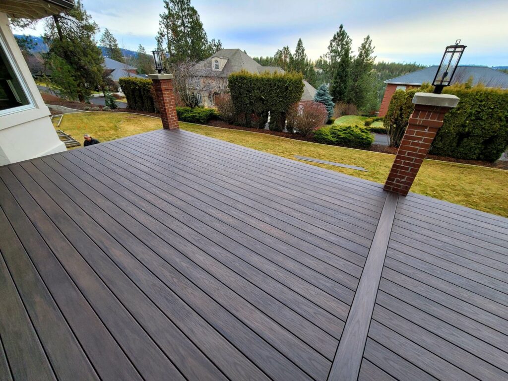 A modern composite deck with decorative brick pillars, offering a view of the neighborhood, installed by Ridgeline Decks in Spokane, WA.