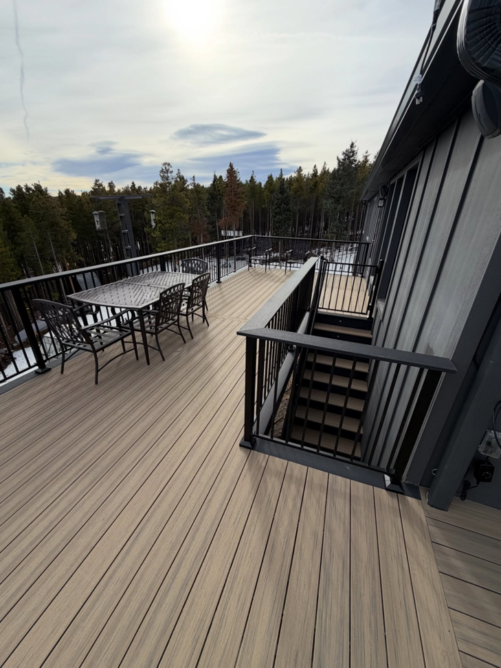 A ground-level view of a composite deck featuring black railings, stairs, and an outdoor dining set by AG - Deck Masters in Arvada, CO.